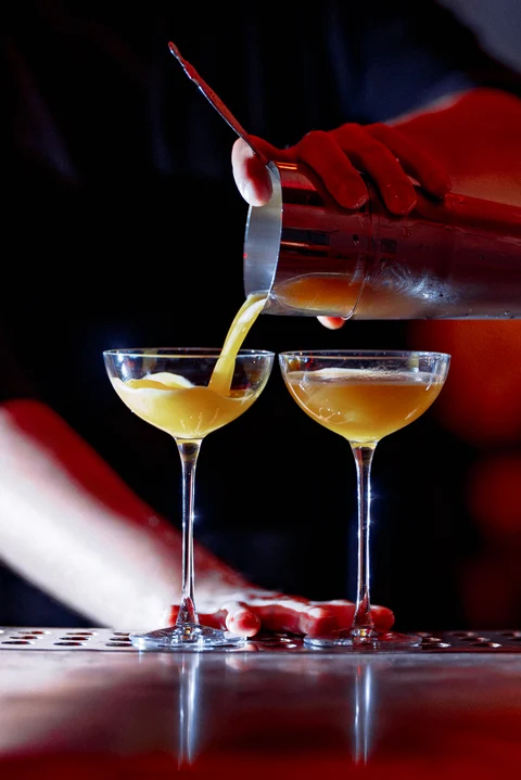 Bartender pouring two golden cocktails